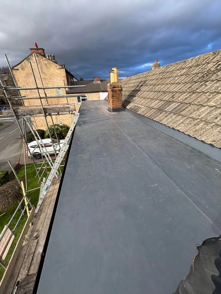Long flat roof extending towards a chimney stack with scaffolding alongside